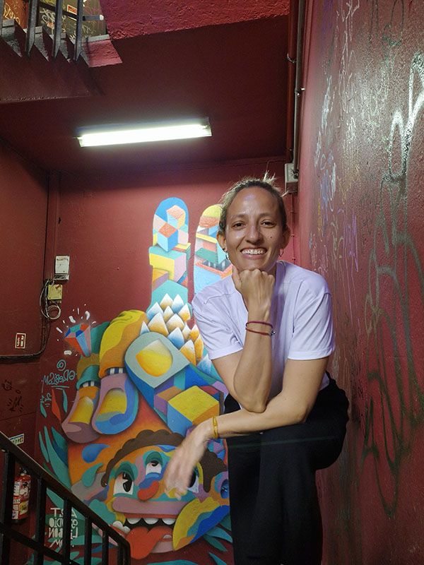 Natalia Méndez sonriendo en unas escaleras de pared roja con murales de arte urbano y graffiti. Lisboa Portugal